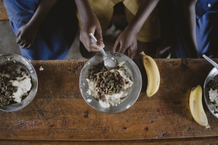 Bikorimana Marcel (center) eats school lunch at EP Kibirizi School in Nyamagabe District