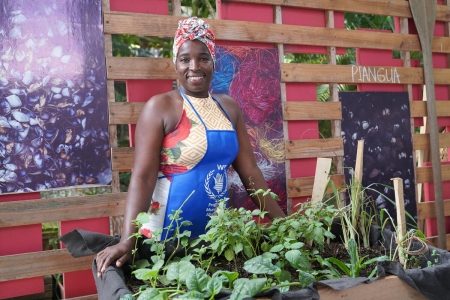 Judith Aguilar, one of the leaders of the workshop of pacific gastronomy, is smiling to the camera while standing behind a small aromatics and spice garden